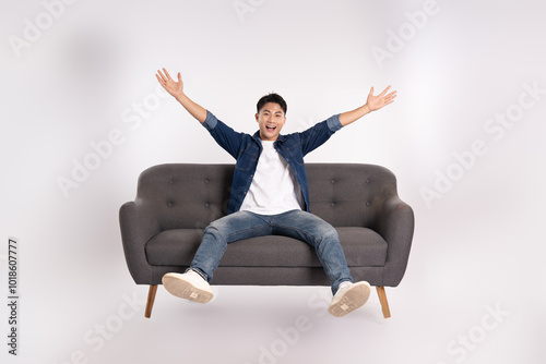 Full body image of young Asian man posing on sofa on white background