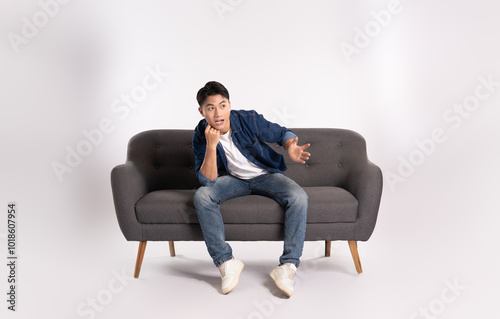 Full body image of young Asian man posing on sofa on white background