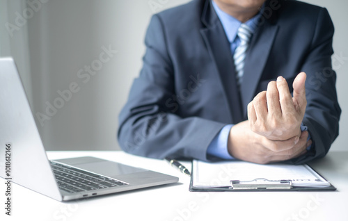 Businessman in office Using a laptop to work so hard that it hurts his wrists, hand massage physiotherapy other side is sore and numb, Guillain-Barre Syndrome, side effect of vaccination