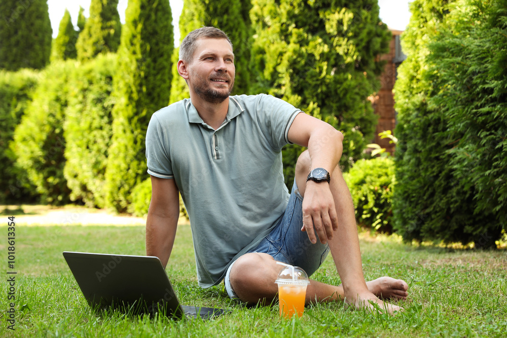 Obraz premium Man with laptop and juice on green lawn outdoors