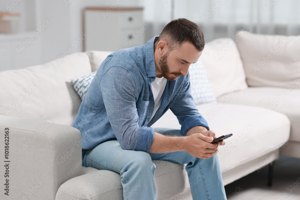 Handsome man using smartphone on sofa indoors Handsome man using smartphone on sofa indoors