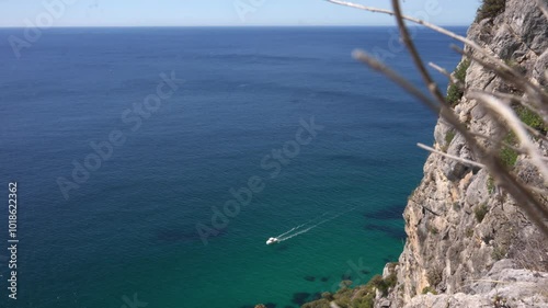 A lone boat leaves a trail across the vast blue ocean, viewed from a high cliffside.