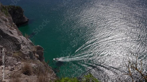 Boat gliding across shimmering turquoise waters viewed from a cliffside perspective.