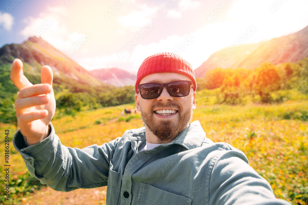Happy hipster tourist man in red hat and sunglasses takes selfie photo on action camera hike against backdrop of volcanoes, Kamchatka trip Happy hipster tourist man in red hat and sunglasses takes selfie photo on action camera hike against backdrop of volcanoes, Kamchatka trip