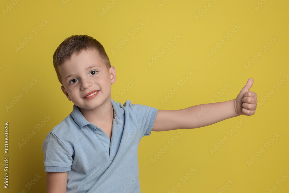 Cute little boy showing thumbs up on yellow background Cute little boy showing thumbs up on yellow background