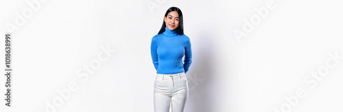 An Asian woman wearing a light blue turtleneck knit sweater and white skinny pants against a white background.