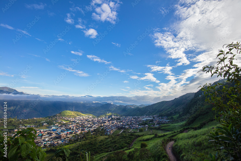 Naklejka premium Fotografía panorámica de un pueblo entre montañas verdes en un cielo azul 