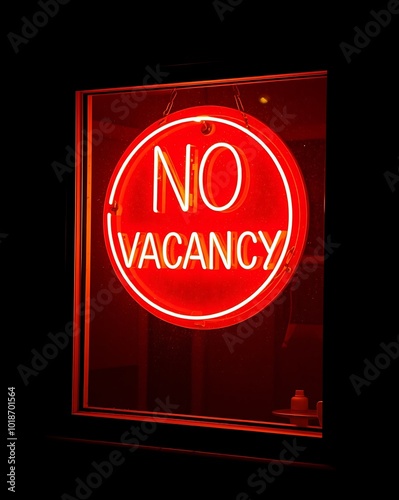 A bold, red No Vacancy sign glows in the window of a motel, illuminating the darkness around it photo