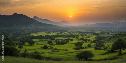 A beautiful sunset over a vast, green field. The sky is filled with clouds, and the sun is setting behind the mountains. The scene is peaceful and serene