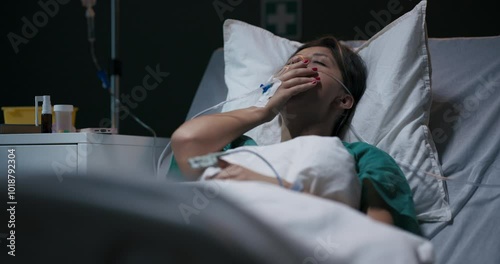 Young ill female patient in hospital ward with tube in nose lying in bed.