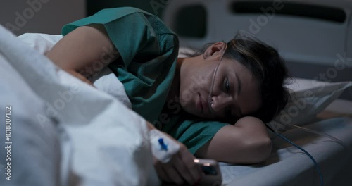 Young woman lying in bed, holding a phone, unable to sleep.