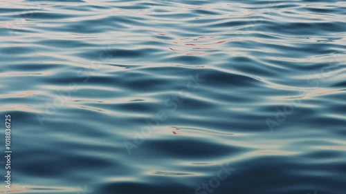 Moving water surface reflects the vibrant red and orange hues of a setting sun. The tranquil scene captures the essence of evening serenity and natural beauty