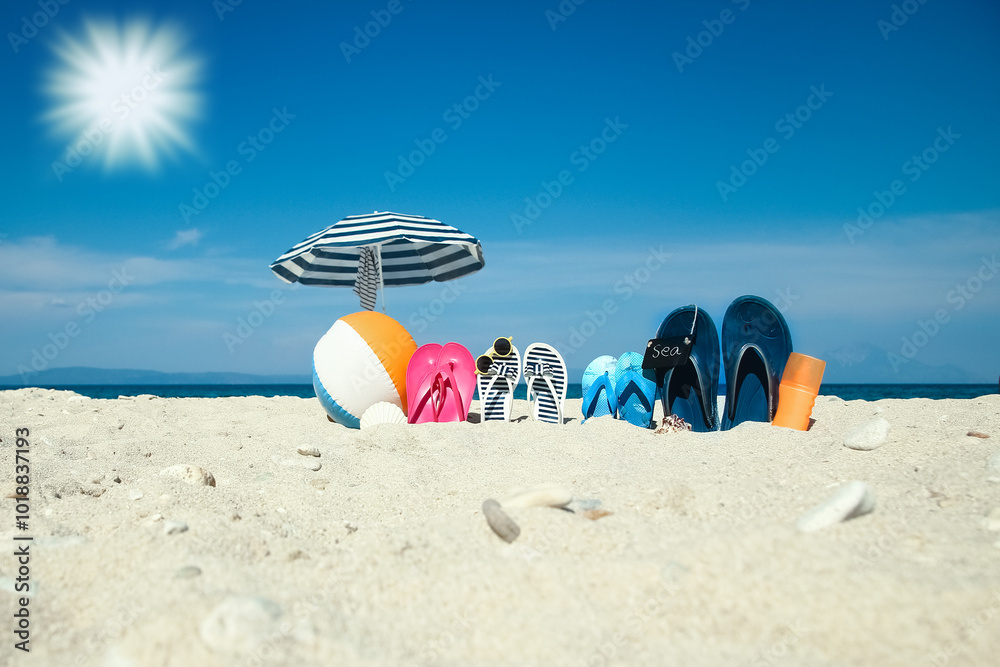 Obraz premium A Beach summer holiday banner background. Flip-flops and hat with a board and ball on the sand near the ocean. Summer accessories on the seashore. 
