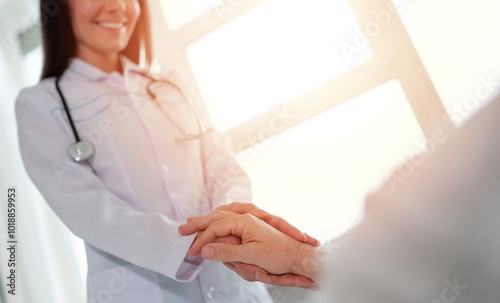 A female doctor in a white coat is gently holding a patient's hand, offering comfort and care. She smiles warmly, conveying trust and compassion in a bright, professional healthcare environment.