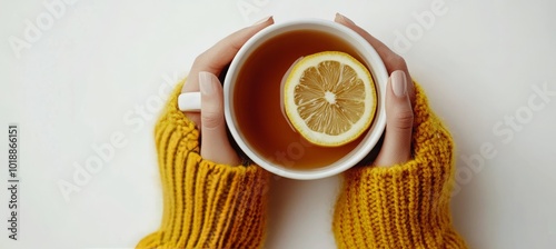 Warm hands holding a cozy cup of tea with lemon while wearing a knitted yello...