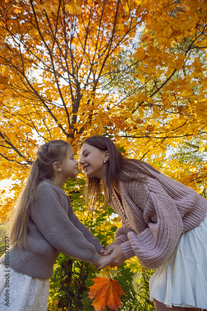 mother and her daughter of seven years walk warm autumn in a park with trees at sunset in orange leaves.