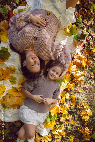 mother and her daughter of seven years walk warm autumn in a park with trees at sunset in orange leaves. lying on the ground among the orange leaves.