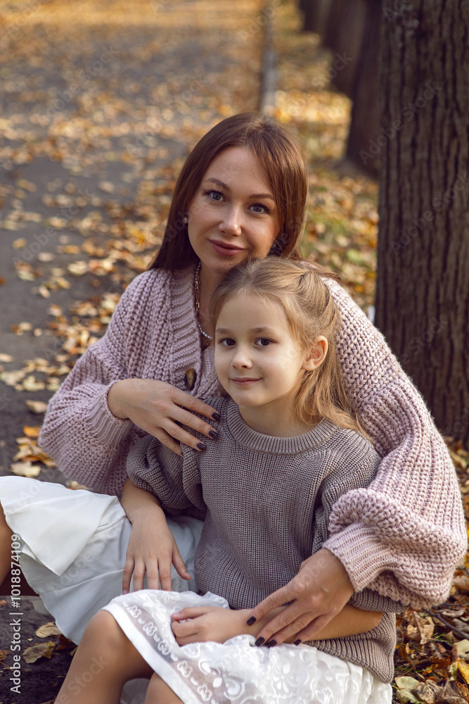 mother and her daughter of seven years walk warm autumn in a park with trees at sunset in orange leaves. sit on the ground among the orange leaves.