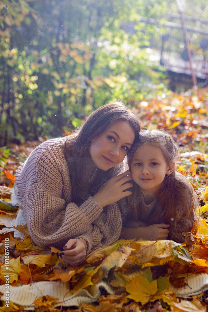 mother and her daughter of seven years walk warm autumn in a park with trees at sunset in orange leaves. lying on the ground among the orange leaves.