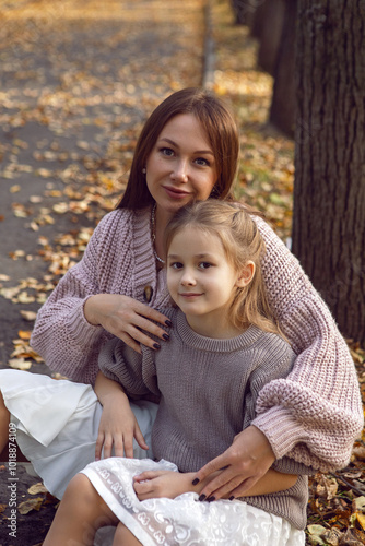 Obraz na płótnie mother and her daughter of seven years walk warm autumn in a park with trees at sunset in orange leaves. sit on the ground among the orange leaves. w salonie