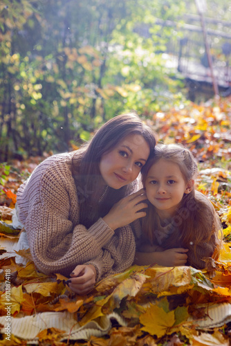 Obraz na płótnie mother and her daughter of seven years walk warm autumn in a park with trees at sunset in orange leaves. lying on the ground among the orange leaves. w salonie
