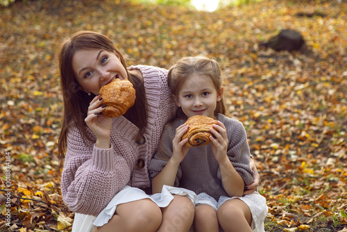 mother and her daughter of seven years walk warm autumn in a park with trees at sunset in orange leaves. sitting on the ground eating croissants.