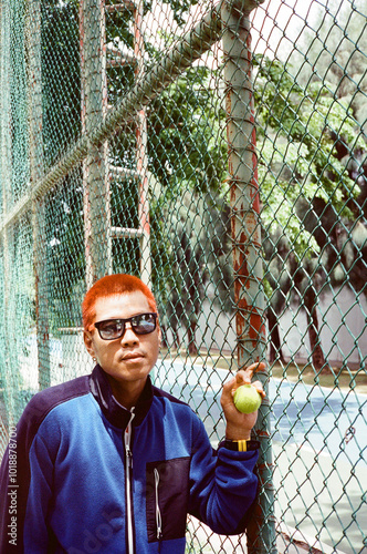 Distinct style hipster guy posing with tennis ball against old fence photo