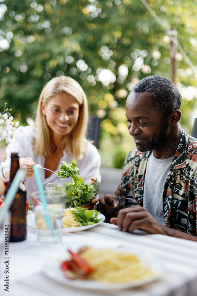 Woman putting salad to boyfriend or husband at table in backyard Woman putting salad to boyfriend or husband at table in backyard