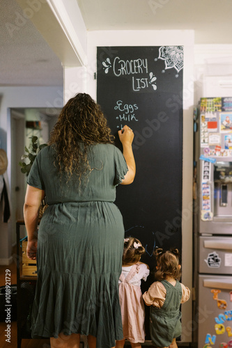 mother writing shopping list in kitchen with toddler daughters  photo