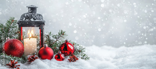 Farol negro conteniendo una vela encendida en su interior, rodeado de bolas de navidad y hojas de abeto, sobre superficie de nieve y fondo gris nevado