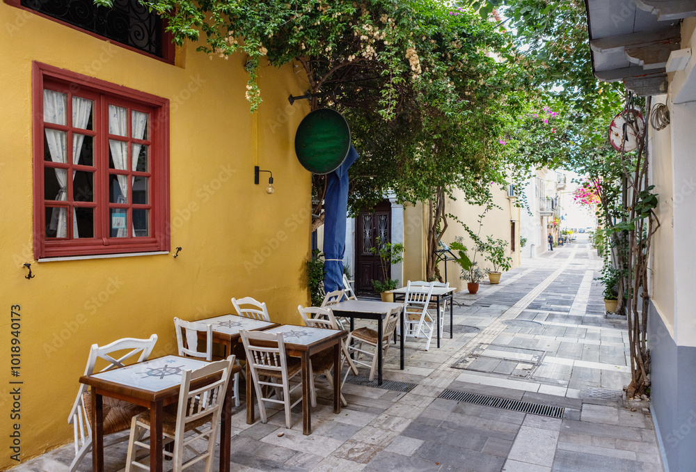 Inviting outdoor tables line a picturesque alley in Nafplio, Greece, where colorful buildings and greenery create a serene atmosphere perfect for leisurely meals. Inviting outdoor tables line a picturesque alley in Nafplio, Greece, where colorful buildings and greenery create a serene atmosphere perfect for leisurely meals.