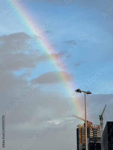 Rainbow Over Urban Skyline with Cranes and Streetlight