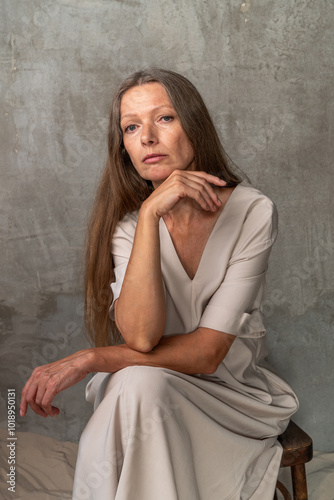 Woman sitting with hand on chin against a concrete wall.

 photo