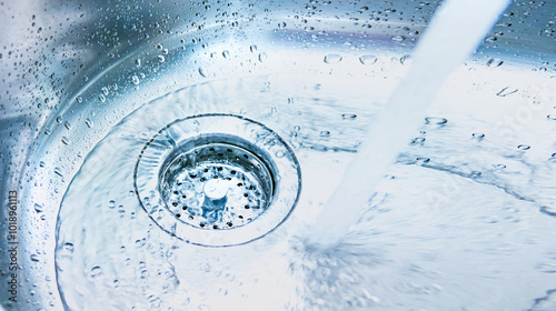 Obraz na płótnie A stream of clean water drink flows into the stainless steel sink. Sink plug hole close up, macro. Environment, water pollution and water shortage concept w salonie