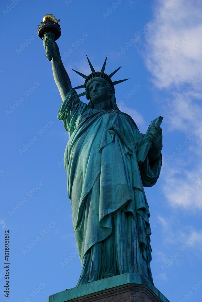 Fototapeta premium Vertikale Ansicht der berühmten Freiheitsstatue von New York, die als Symbol amerikanischer Freiheit eine Fackel hochhebt vor klarem blauen Himmel