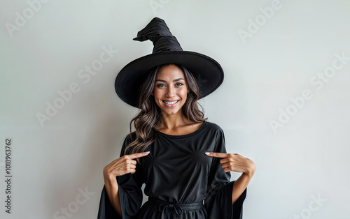 Woman in Halloween witch costume pointing with her finger agaist neutral background with copy space photo