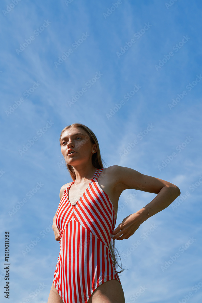 Woman Adjusting Red Striped Swimsuit Under Clear Sky Woman Adjusting Red Striped Swimsuit Under Clear Sky