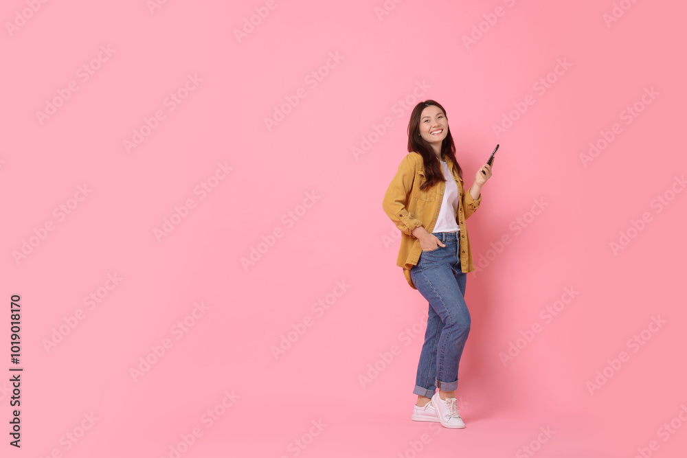 Smiling young woman with smartphone on pink background. Space for text Smiling young woman with smartphone on pink background. Space for text