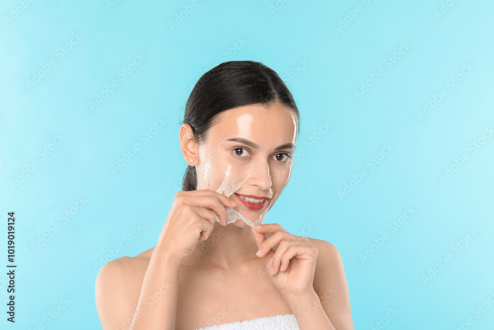 Smiling woman peeling off face mask on light blue background Smiling woman peeling off face mask on light blue background