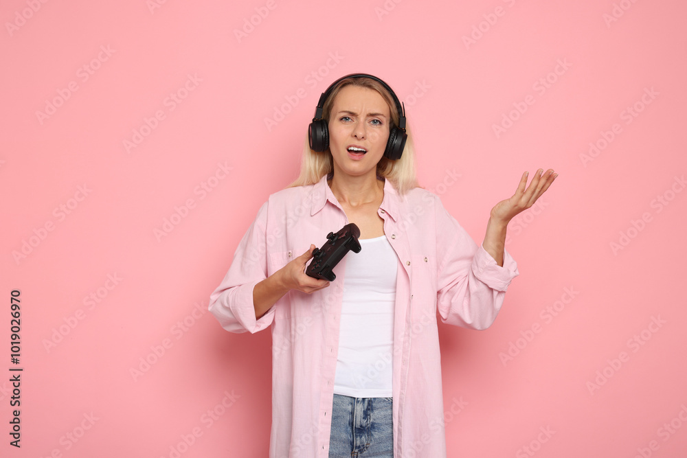 Unhappy woman in headphones playing video games with controller on pink background Unhappy woman in headphones playing video games with controller on pink background