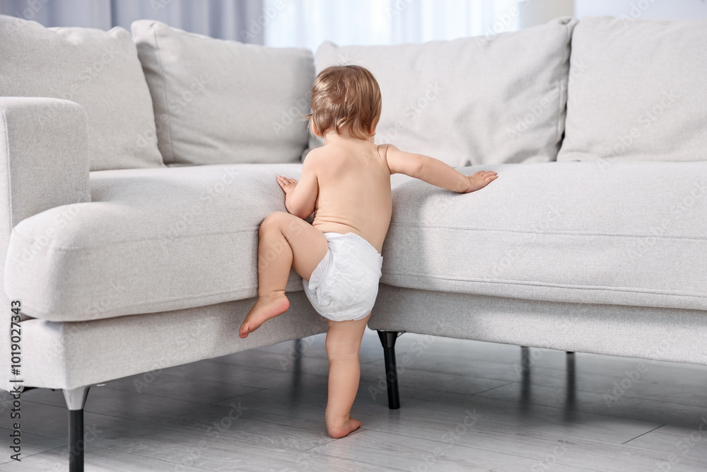 Little child in diaper climbing on sofa at home, back view Little child in diaper climbing on sofa at home, back view