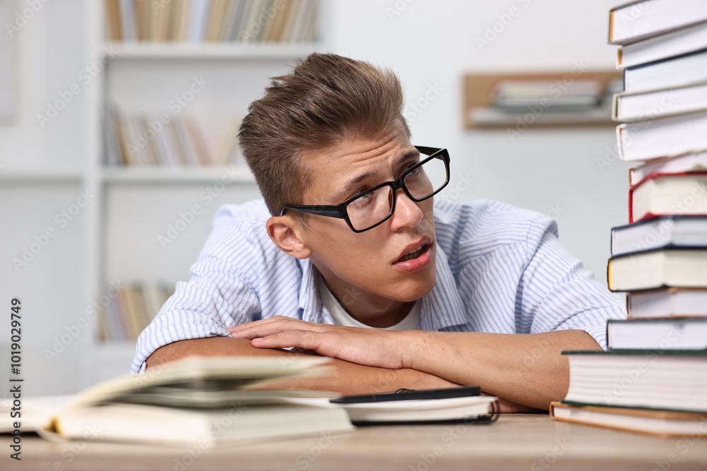 Tired student before exam with stack of books at table indoors Tired student before exam with stack of books at table indoors