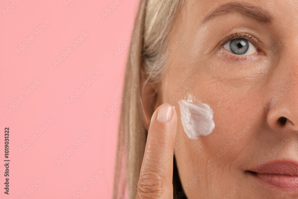 Senior woman applying face cream on pink background, closeup. Space for text Senior woman applying face cream on pink background, closeup. Space for text