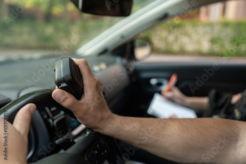 Police officer driving car holding radio and talking with partner taking notes