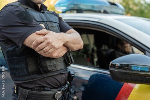 Police officer standing with arms crossed by patrol car photo