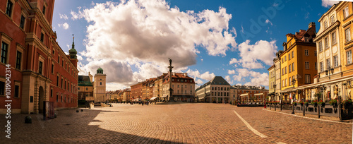 Obraz na płótnie Panoramic view of Warsaw's historic market square under a vibrant blue sky with scattered clouds, showcasing colorful historic buildings and a lively atmosphere. w salonie
