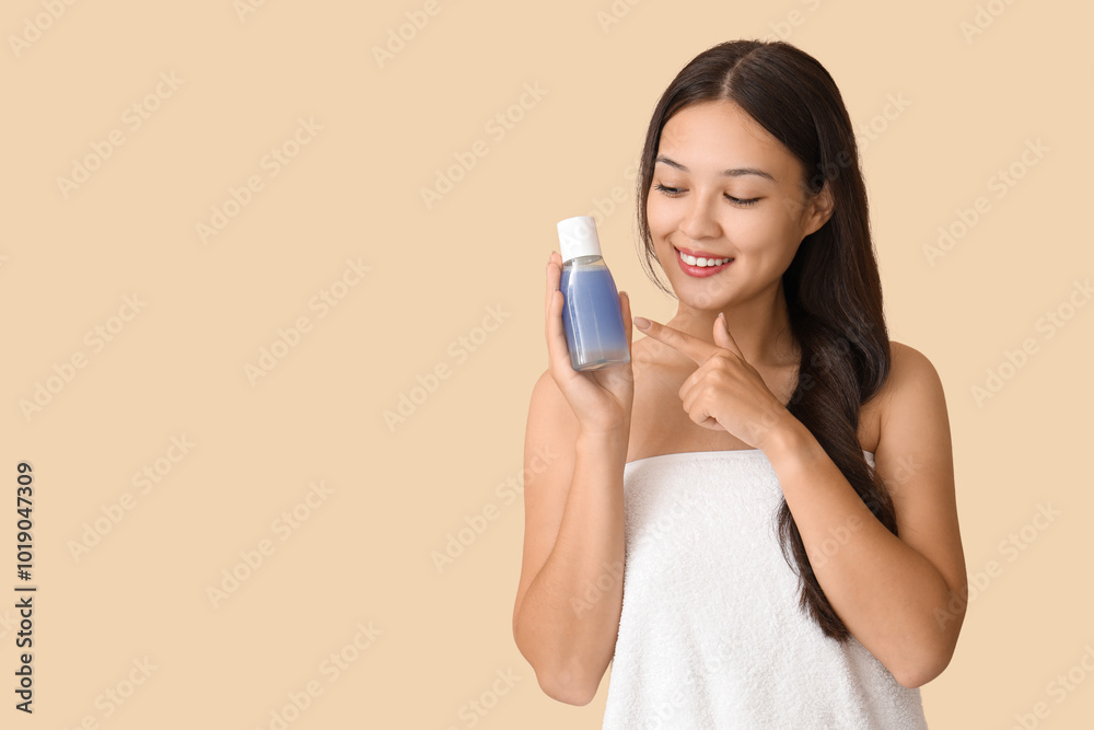 Young Asian woman pointing at bottle of micellar water on beige background Young Asian woman pointing at bottle of micellar water on beige background