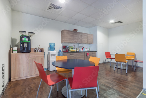 A room in a modern office for relaxing and snacking. A small kitchen set, a cooler and .a coffee machine. Round tables and colorful chairs.