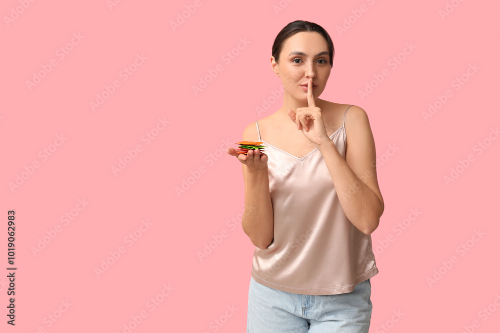 Beautiful young woman with condoms showing silent gesture on pink background. Safe sex concept Beautiful young woman with condoms showing silent gesture on pink background. Safe sex concept