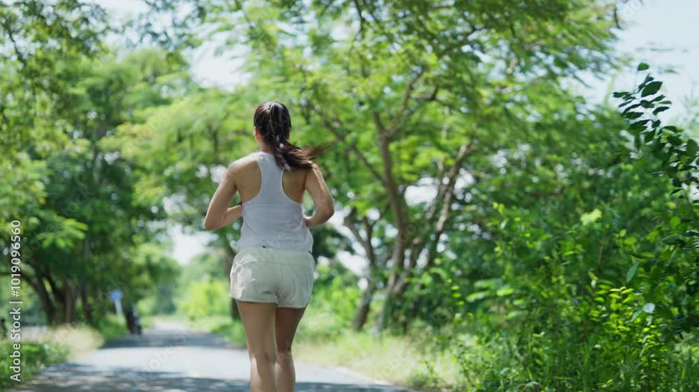 A woman is running in a forest. The trees are green and the sky is blue. The woman is wearing a white tank top and white shorts A woman is running in a forest. The trees are green and the sky is blue. The woman is wearing a white tank top and white shorts